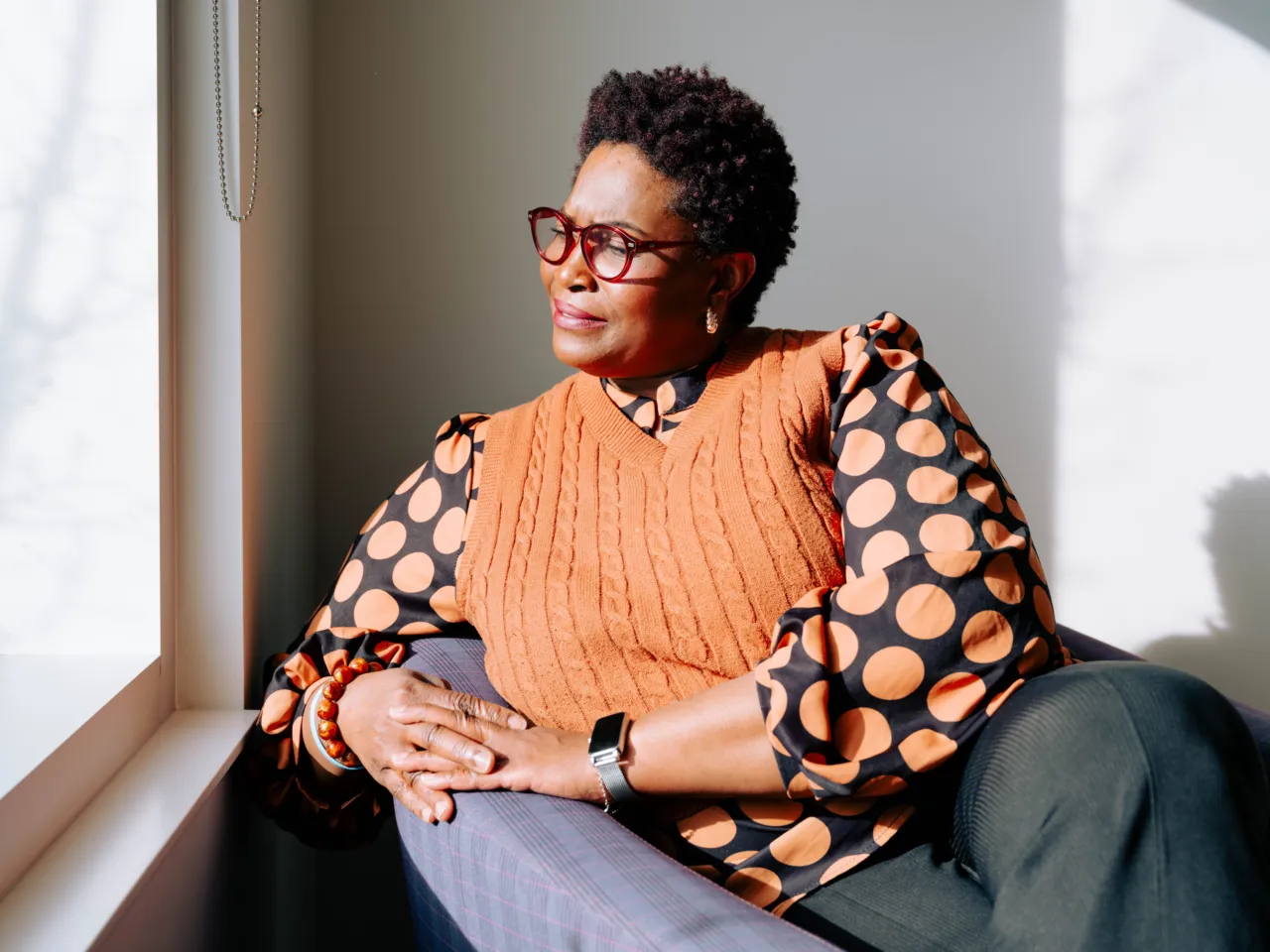 Woman with glasses sitting thoughtfully by a sunlit window